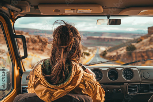 A woman with long hair is driving a yellow truck on a road. The woman is wearing a yellow jacket and has her hair in a ponytail. The truck is parked on a road with a mountain in the background