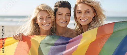 Happy woman friends showing pride flag for equality and standing together on the beach.