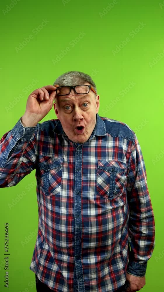Senior man in casual clothing raises glasses looks camera with surprised face. Senior man in casual clothing raises glasses looks camera with surprised face.