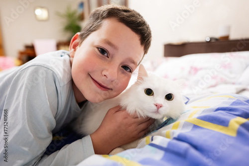 A cheerful young boy hugging his fluffy white cat while lying on a colorful bedspread, portraying companionship and love.