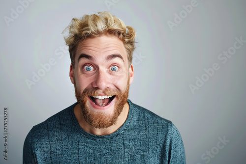A very excited, surprised man looks at the camera with his mouth open, isolated on a light gray background. A funny-looking red-haired and bearded man. Live emotions. Idea for advertising. Copy space