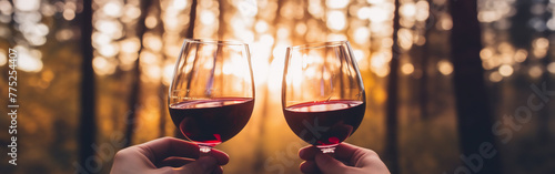 Two female hands toasting or clinking with red wine glasses on a forest and minimalist background 