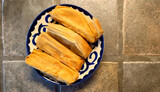 four pork tamales still in the husk on a painted blue and white plate on a porcelain tiled countertop 