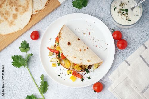 Plate of tasty pita bread with grilled vegetables and sauce on white background photo