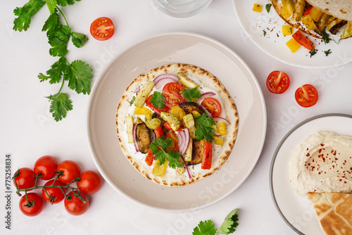 Plates of tasty pita bread with grilled vegetables on white background photo