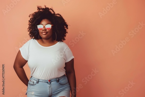 plus sized young woman wearing holographic sunglasses blank white tshirt and casual jeans against a pastel peach backdrop, design mockup