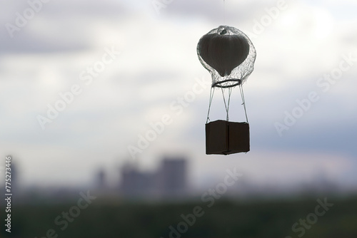 silhouette of a mini aerostat with a basket and a head of garlic in the form of a ball against the background of blurred contours of the urban landscape