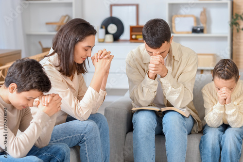 Family with Holy Bible praying on sofa at home © Pixel-Shot