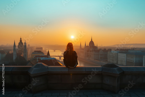 Silhouette of a person watching sunrise over a cityscape.