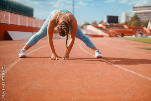 A sportswoman is stretching on stadium and preparing for exercise.