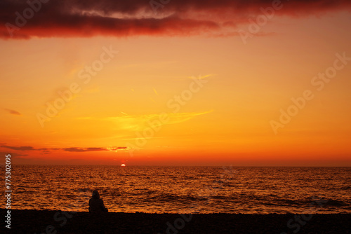 Orange sky background with clouds at sunset and black silhouettes of people against the sky and sea on a summer evening. Seascape	