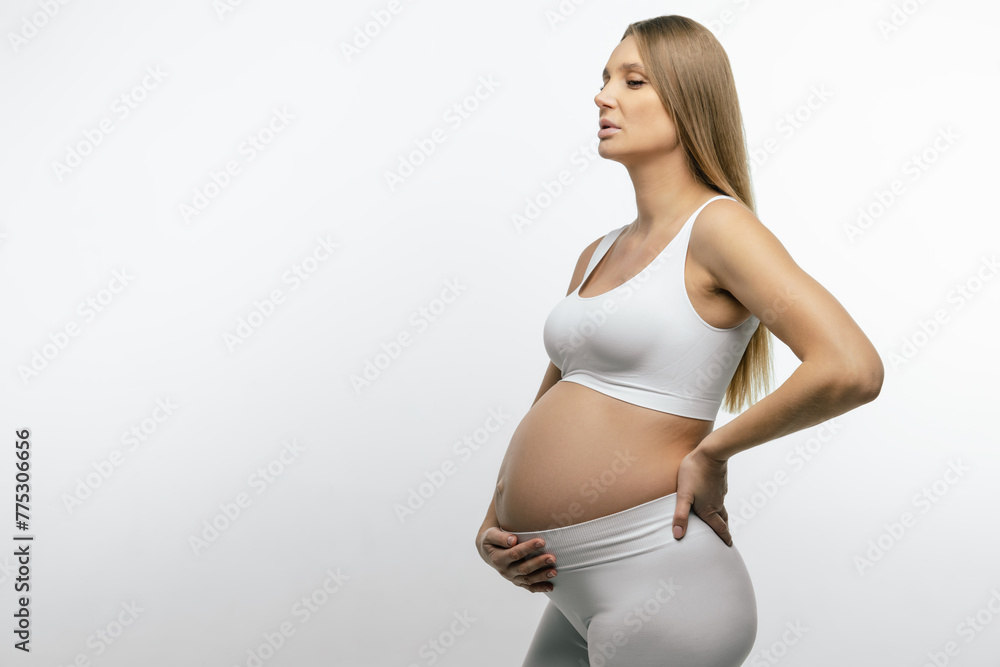 Pregnant woman in white top and leggings holding her hand on her belly Pregnant woman in white top and leggings holding her hand on her belly