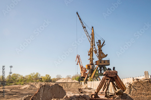 Port industrial cranes at river sand unloading depot on clear sunny day