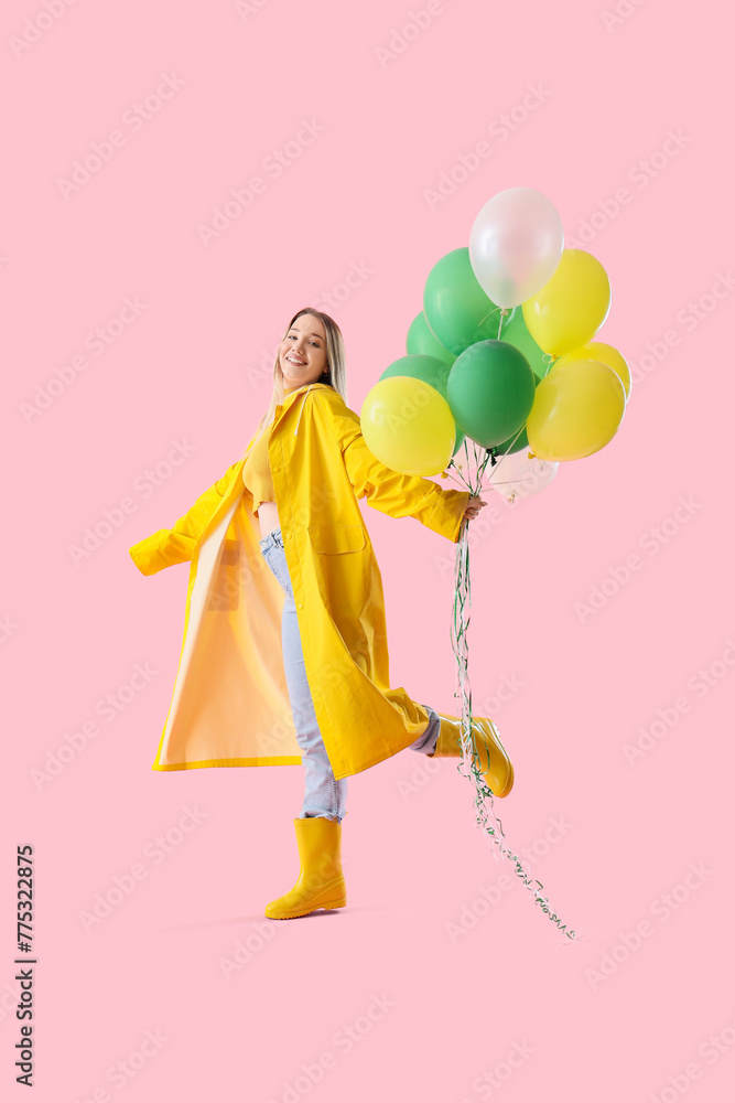 Young woman in raincoat with balloons on pink background