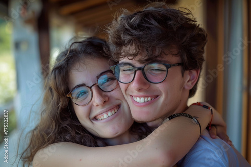 A boy and a girl wearing glasses are hugging and smiling