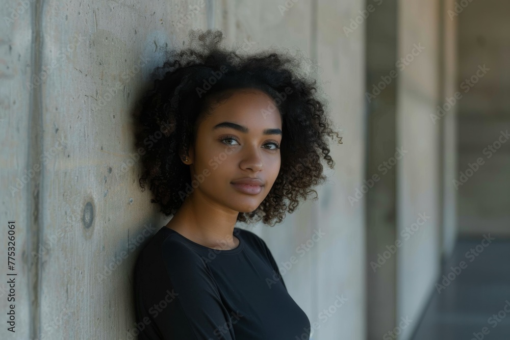 A portrait of an attractive young woman with curly hair, leaning against a rough textured concrete wall A portrait of an attractive young woman with curly hair, leaning against a rough textured concrete wall