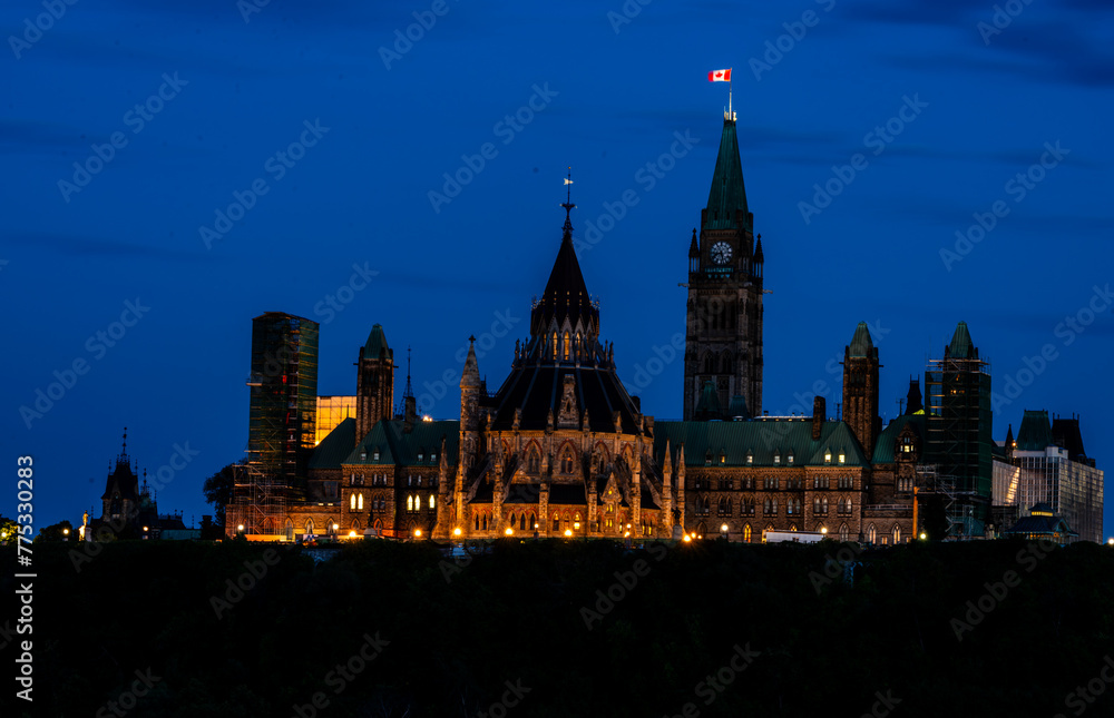 The Canadian Parliament buildings at dusk, in Ottawa, Canada.  The Canadian flag is brightly illuminated at the top of the peace tower.