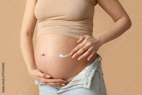 Young pregnant woman with cream against stretch marks on beige background, closeup © Pixel-Shot