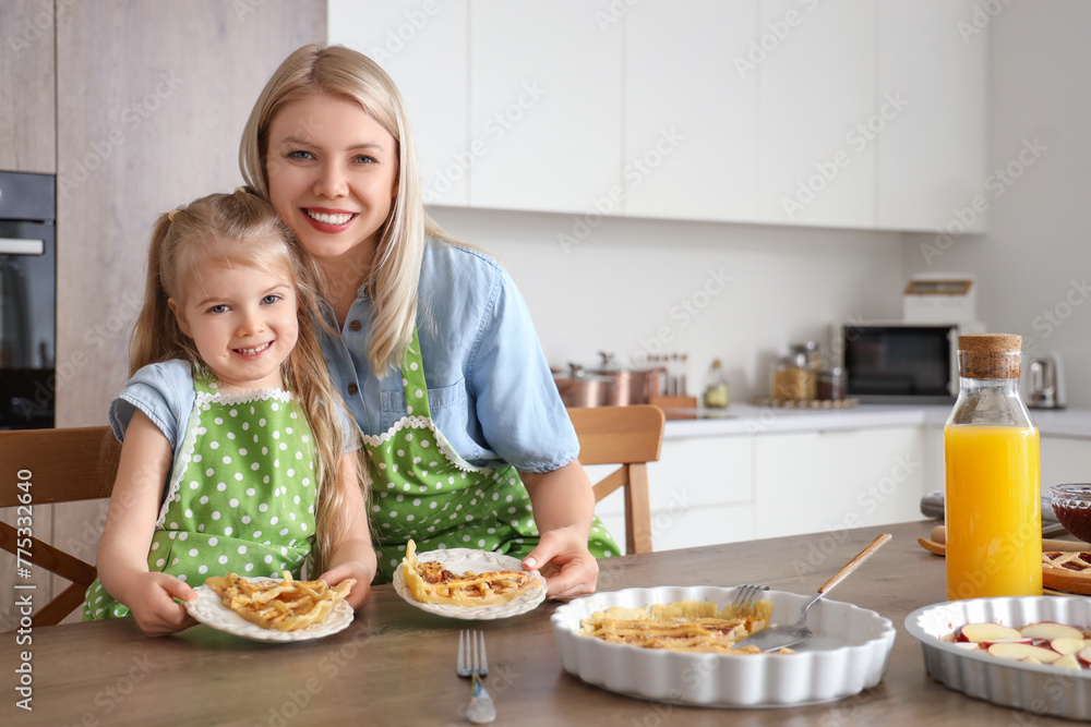 Cute little girl and her mother with prepared apple pie hugging in kitchen