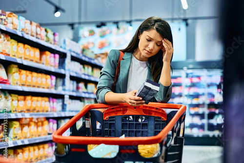 Mid adult woman feeling worried about grocery prices while shopping in  supermarket.