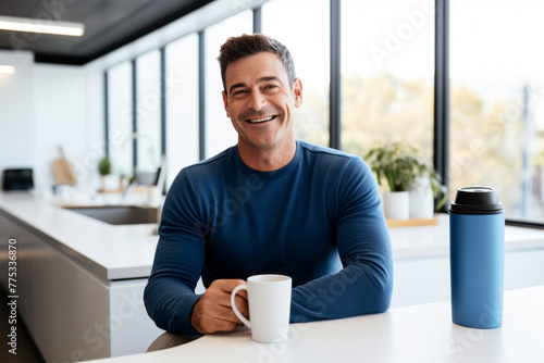A happy cheerful man smiling at camera enjoying coffee break sitting in modern office kitchen.