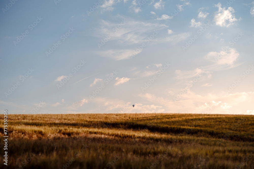 Einsamer kleiner Heißluftballon am Horizont über einem Feld bei Sonnenuntergang