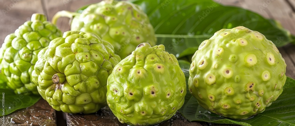 Obraz premium A group of green fruits sit on a wooden table with leaves, next to a leafy green plant