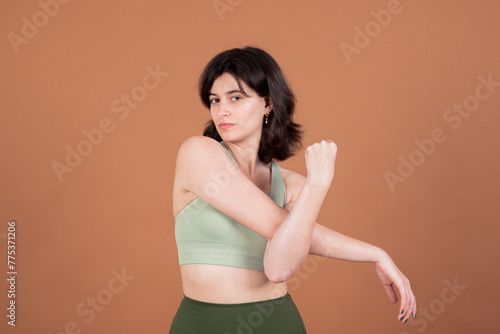 A young woman stretches her arms while posing in green sportswear and looking directly at the camera, exuding determination and vitality.