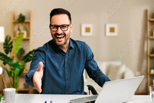 Handsome business man with a smile on his face is sitting at a desk and extending his hand for a handshake