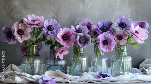  Row of vases with purple, pink flowers on white cloth table near gray wall