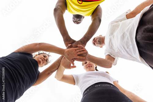 From a unique low angle, a basketball team's hands join together above, symbolizing team spirit and shared goals before the game