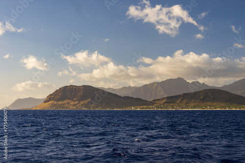 a beautiful spring landscape of the coast of Oahu with majestic mountain ranges, lush green trees and plants, rippling blue ocean water and blue sky with clouds at sunset in Kapolei Hawaii USA photo