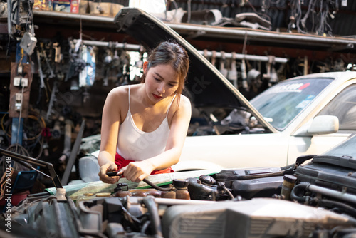 Female Mechanic Working Under Vehicle in a Car Service. Empowering Woman Wearing Gloves and Using a Ratchet Underneath the Car. Modern Clean Workshop.
