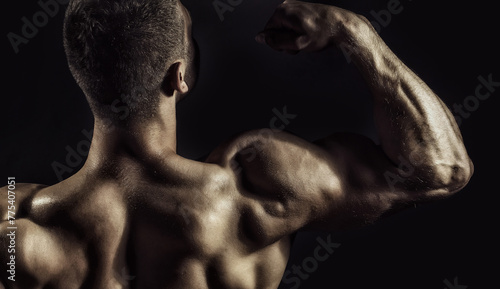 biceps and shoulder back. Muscular man with sexy body. Sexy muscular male back of athlete bodybuilder posing in power with raised hands and bare torso on dark background.