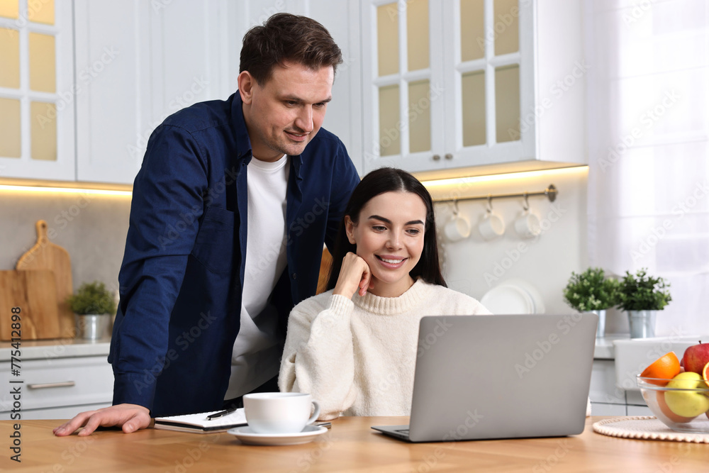Happy couple using laptop together at wooden table in kitchen Happy couple using laptop together at wooden table in kitchen