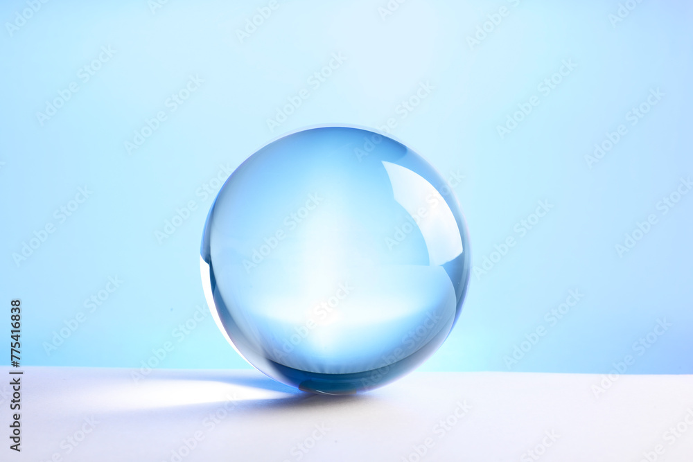 Transparent glass ball on table against light blue background Transparent glass ball on table against light blue background