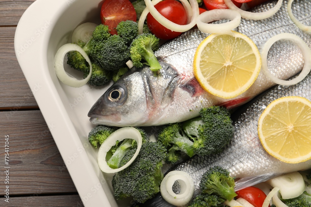 Raw fish with vegetables and lemon in baking dish on wooden table, top view Raw fish with vegetables and lemon in baking dish on wooden table, top view