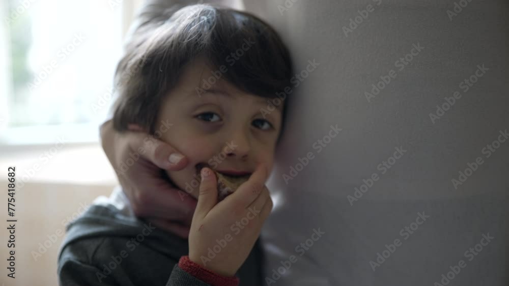 Small boy eating slice of bread while receiving affection from mother's hand. Close-up of 5 year old child leaning on mom while snacking in authentic family scene Small boy eating slice of bread while receiving affection from mother's hand. Close-up of 5 year old child leaning on mom while snacking in authentic family scene