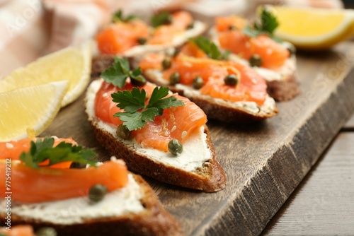 Tasty canapes with salmon, capers, lemon and cream cheese on wooden table, closeup