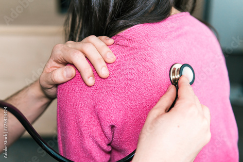 Over the shoulder view of anonymous physician using a stethoscope on patient's back, listening for clear lung sounds in a medical exam photo
