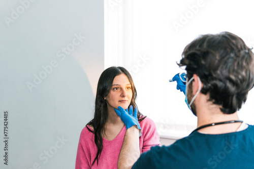 A medical professional in gloves palpates the neck of a patient, checking for swollen lymph nodes in a routine exam photo