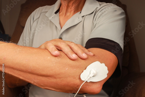 Man using an Electro Therapy Massager or Tens Unit on his elbow for pain relief of Muscles and Joint