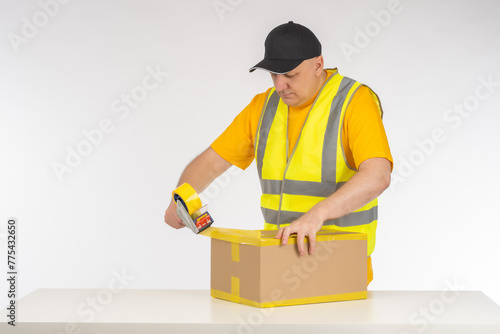 Man packer at work. Warehouse worker seals box with tape. Dispenser with tape in hands man. Packer guy is near table. Businessman is preparing parcel for shipment. Packer of goods from online store photo