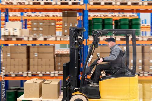 Man storekeeper on forklift. Driver warehouse truck. Forklift drives past parcel racks. Storekeeper transports pallet with boxes. Man works in logistics center. Distribution, fulfillment. Art focus
