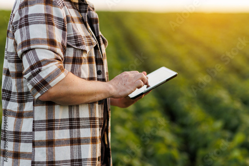 Modern agribusiness. Unrecognisable male farmer uses digital tablet for analyse, checks soybeans plantation. Smart farming technology. Quality control growth and development of sprouts before harvest