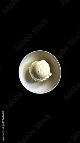 A single, perfect scoop of vanilla ice cream in a classic white bowl, centered against a stark, matte black background. The contrast emphasizes the purity and simplicity of the ice cream, drawing the