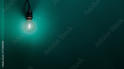 Single Light Bulb Glowing Dimly in a Dark Room with a Teal Wall: A medium shot of a single, dimly glowing light bulb in a dark room, with a teal wall in the background, illustrating the isolation and