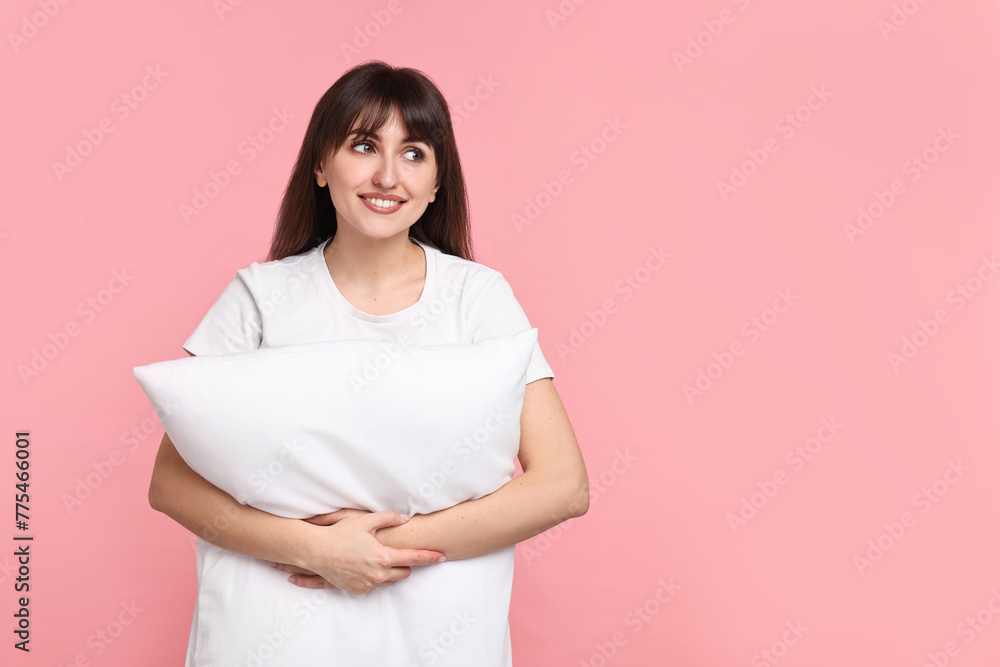 Fototapeta premium Happy woman in pyjama holding pillow on pink background, space for text
