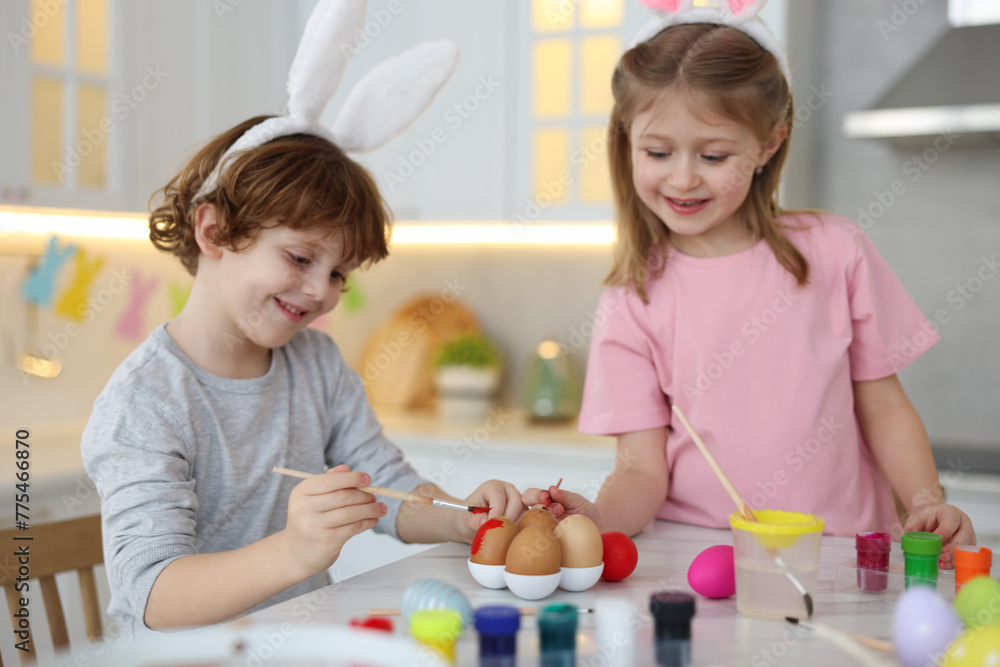 Easter celebration. Cute children with bunny ears painting eggs at white marble table in kitchen Easter celebration. Cute children with bunny ears painting eggs at white marble table in kitchen