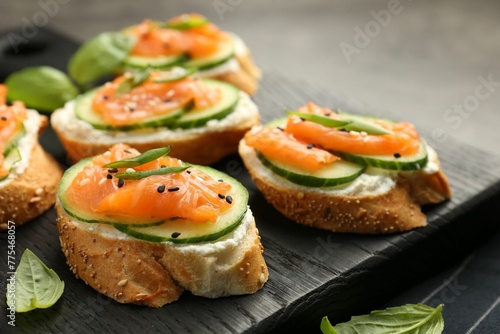 Tasty canapes with salmon, cucumber and cream cheese on table, closeup